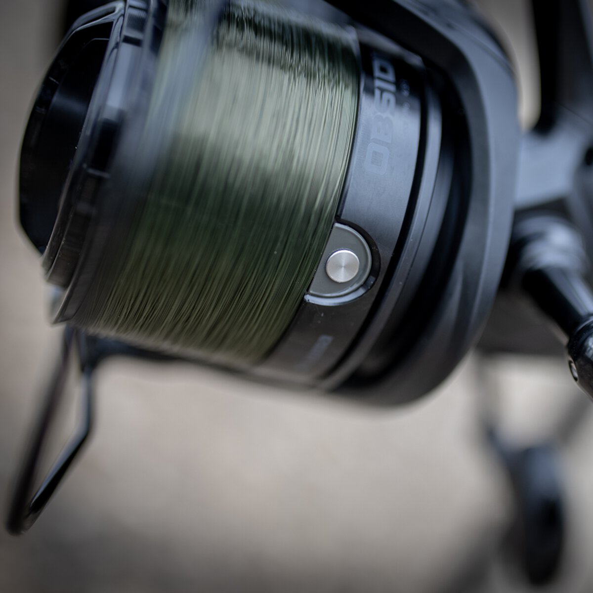 Close-up of the Obsidian's deep aluminium spool packed with green mono, with the line clip stud on the spool lip