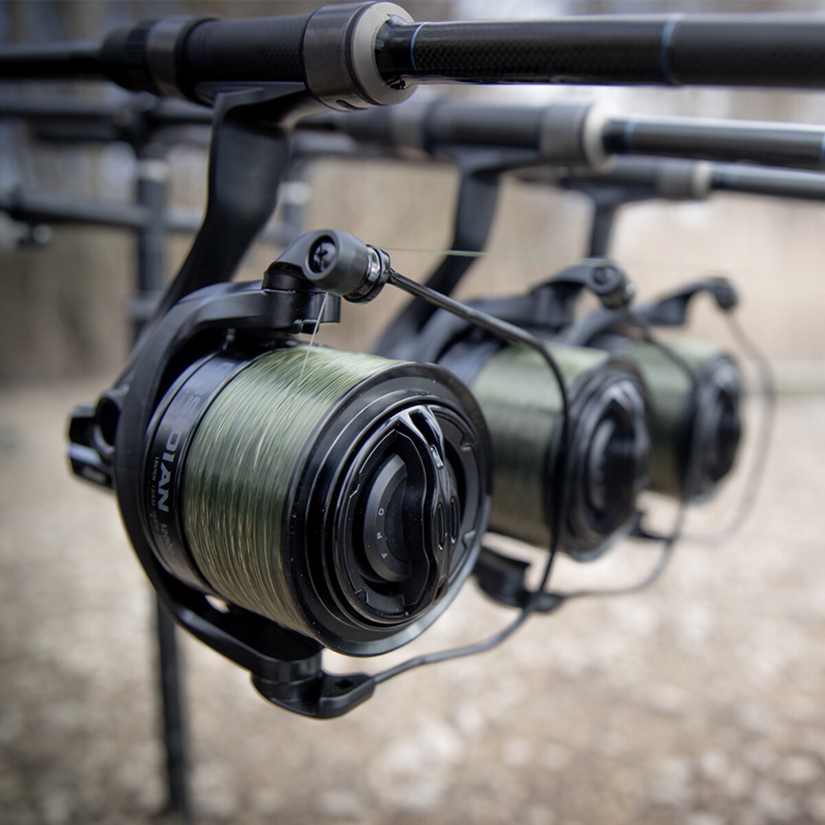 Three Obsidian big-pit reels loaded with green mono, mounted on carp rods sat on a rod pod at the bank
