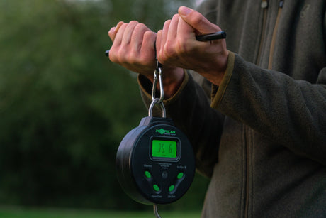 Angler holding the digital scale on a weigh bar through a carabiner, backlit display reading 36.6 lbs at the bank