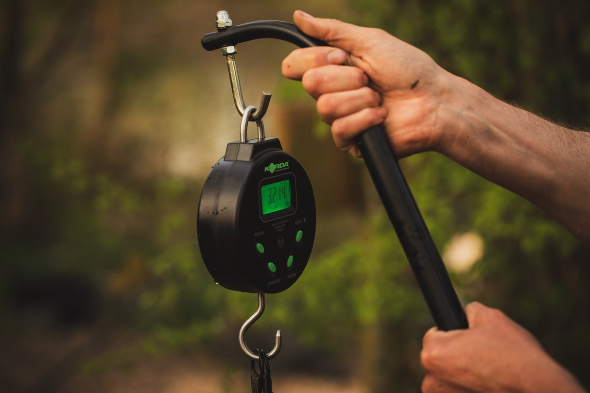Side profile of the scale hung from a weigh bar, showing the depth of the case, the top loop and the stainless bottom hook