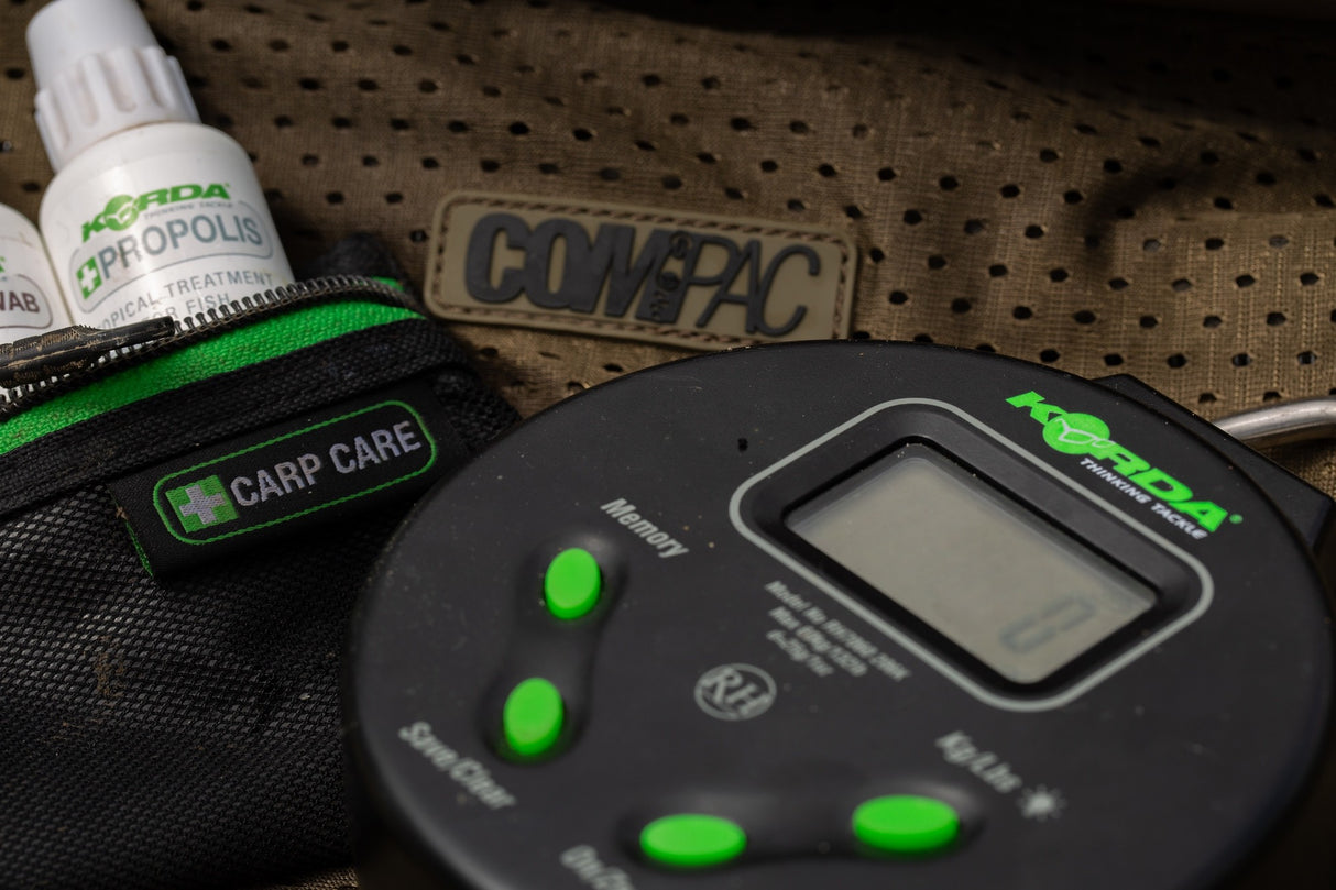 The digital scale resting on an unhooking mat beside a Korda carp care pouch and Propolis treatment bottle