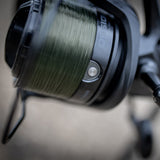 Close-up of the Obsidian's deep aluminium spool packed with green mono, with the line clip stud on the spool lip