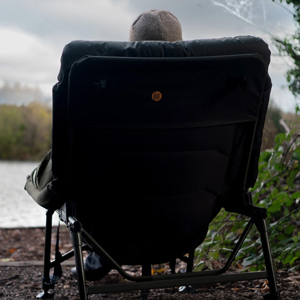 Rear three-quarter with the angler seated, gold Worldwide globe badge centred on the back panel, one arm and the frame bracing visible.