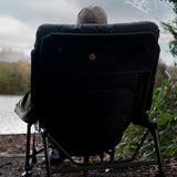 Rear three-quarter with the angler seated, gold Worldwide globe badge centred on the back panel, one arm and the frame bracing visible.
